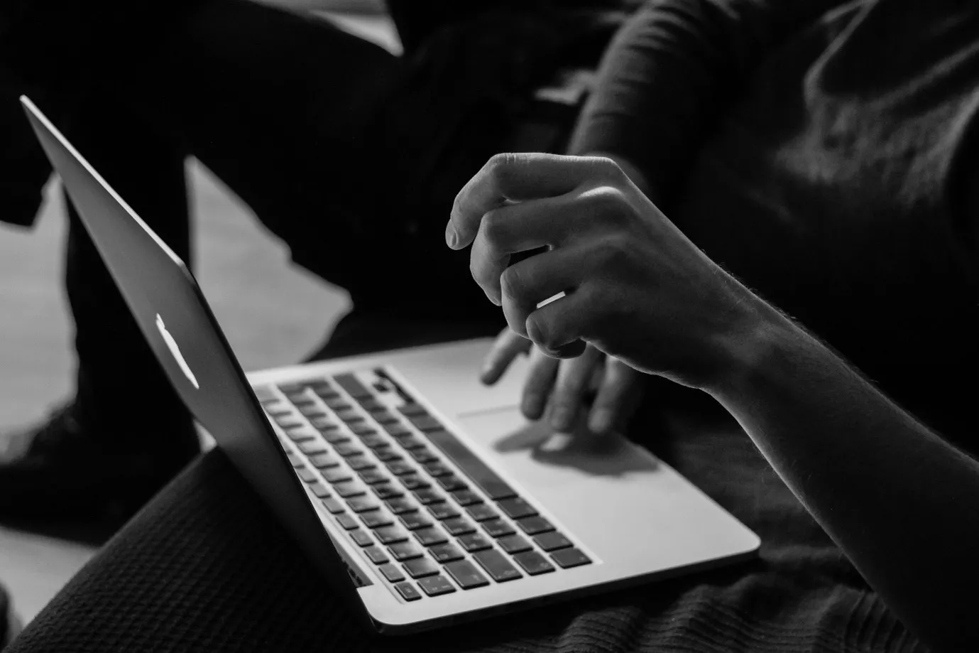 Person using a laptop, typing and gesturing with one hand, in a black and white photo.